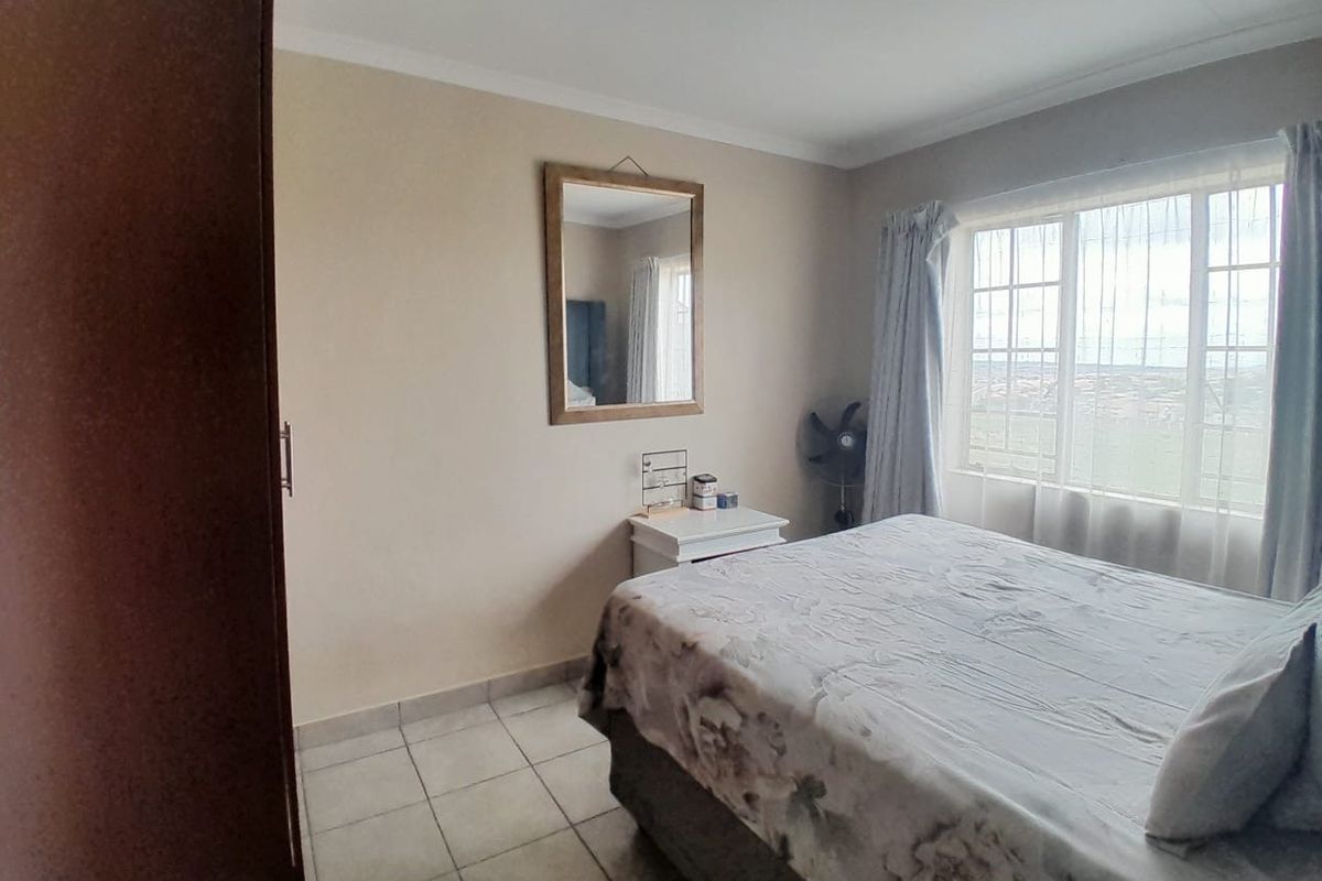 A functional bedroom featuring tiled flooring, a built-in wardrobe, and a window with security bars, offering a neutral space ready for personalization.