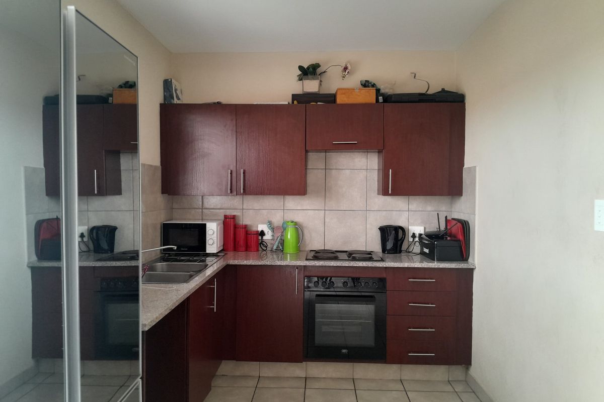 A functional kitchen featuring dark wood cabinetry, granite-look laminate countertops, a built-in oven, electric hob, and neutral tiled backsplash and flooring.