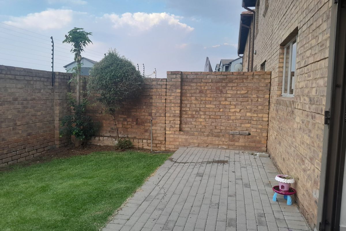 A private rear courtyard featuring a paved patio area, a small lawn, and secure brick boundary walls with electric fencing.