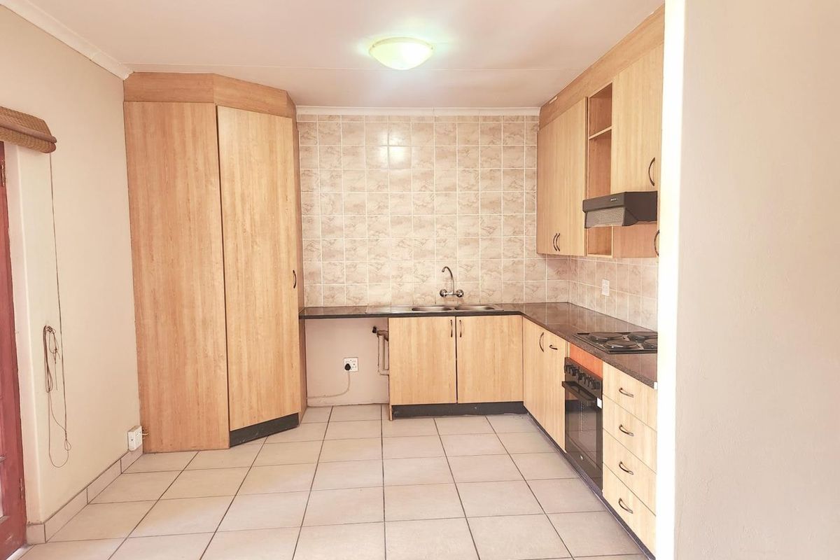 A functional kitchen featuring light wood-finish cabinetry, tiled backsplash, built-in oven, hob, and extractor fan with neutral floor tiles.