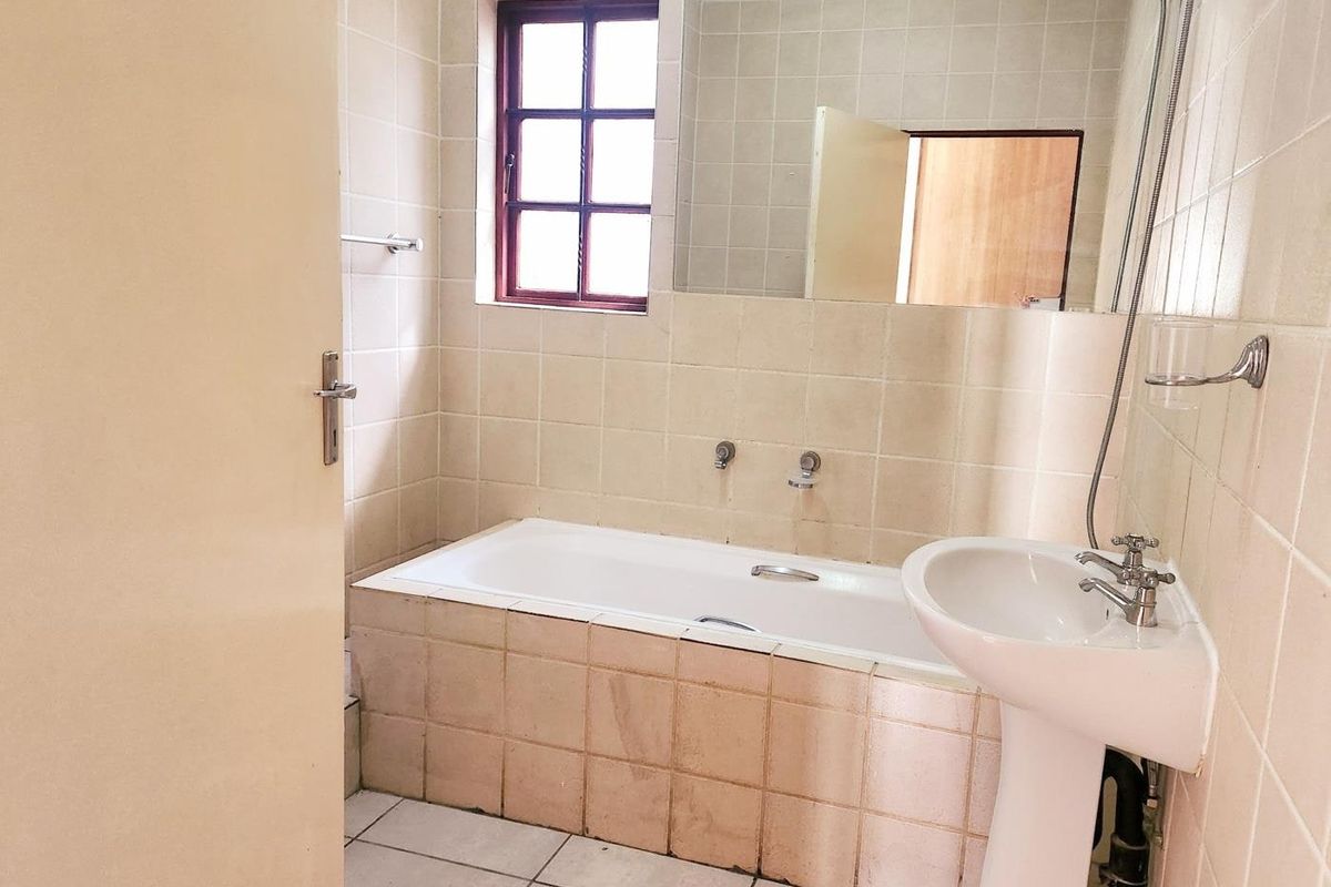 A dated bathroom featuring a built-in bathtub, pedestal basin, and wall-to-wall tiling, offering a functional space ready for modernization.