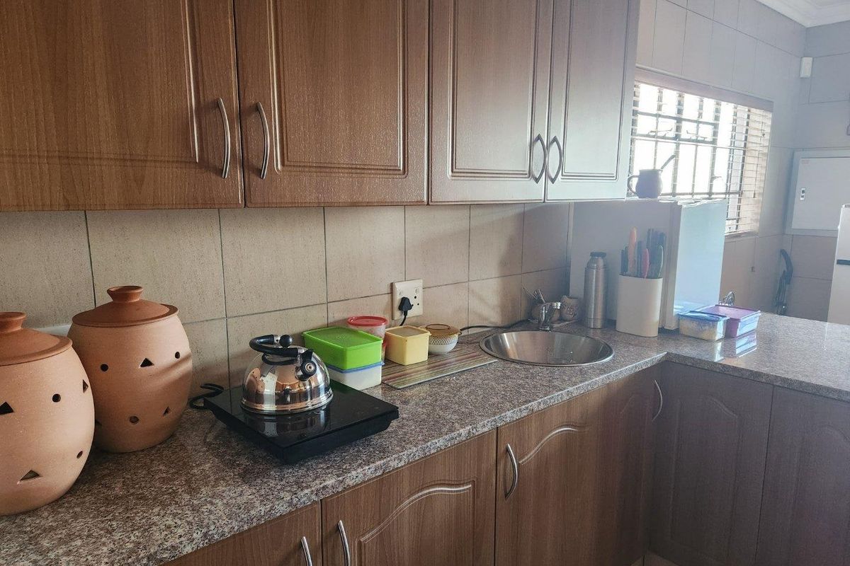 A functional kitchen featuring wood-look cabinetry, granite countertops, and a stainless steel sink with tiled backsplash.