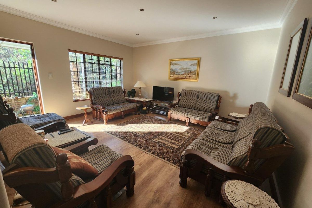 A spacious living room featuring laminate flooring, recessed downlights, and direct access to the exterior through a security gate.