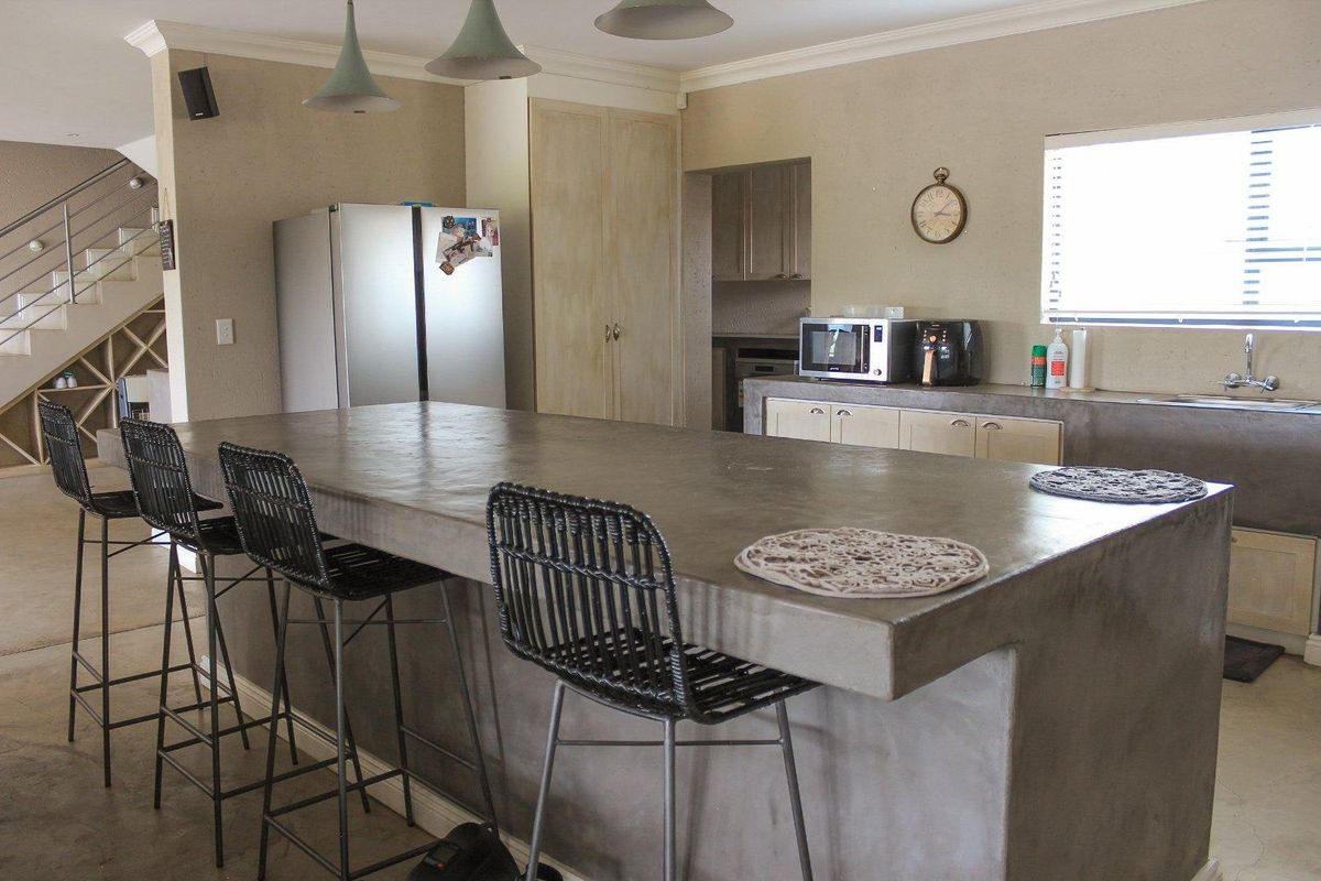 Spacious kitchen featuring a large concrete island, custom cabinetry, and integrated sink, with an adjacent staircase leading to the upper level.