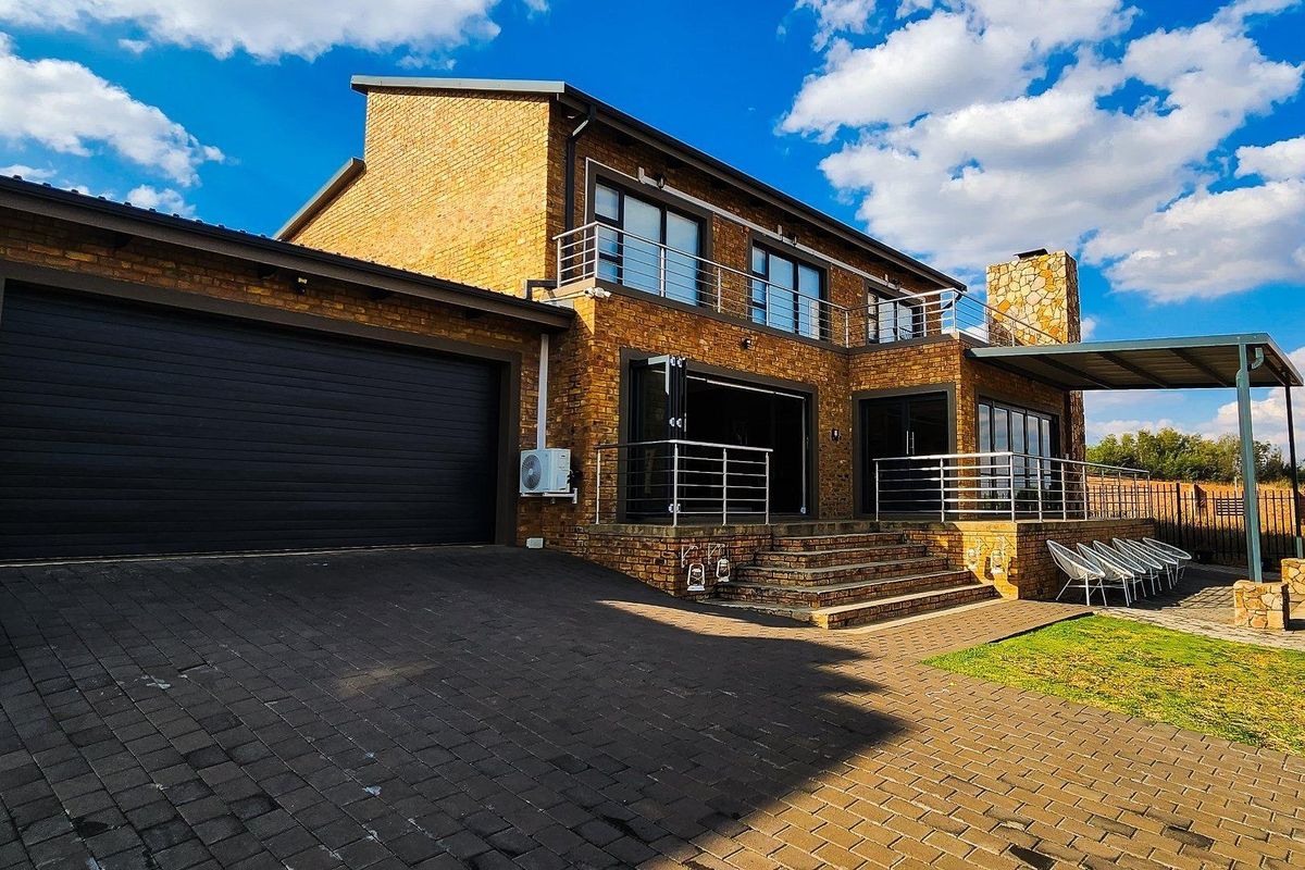 A modern double-story face brick home featuring a double garage, spacious balcony with stainless steel balustrades, and a covered patio area.