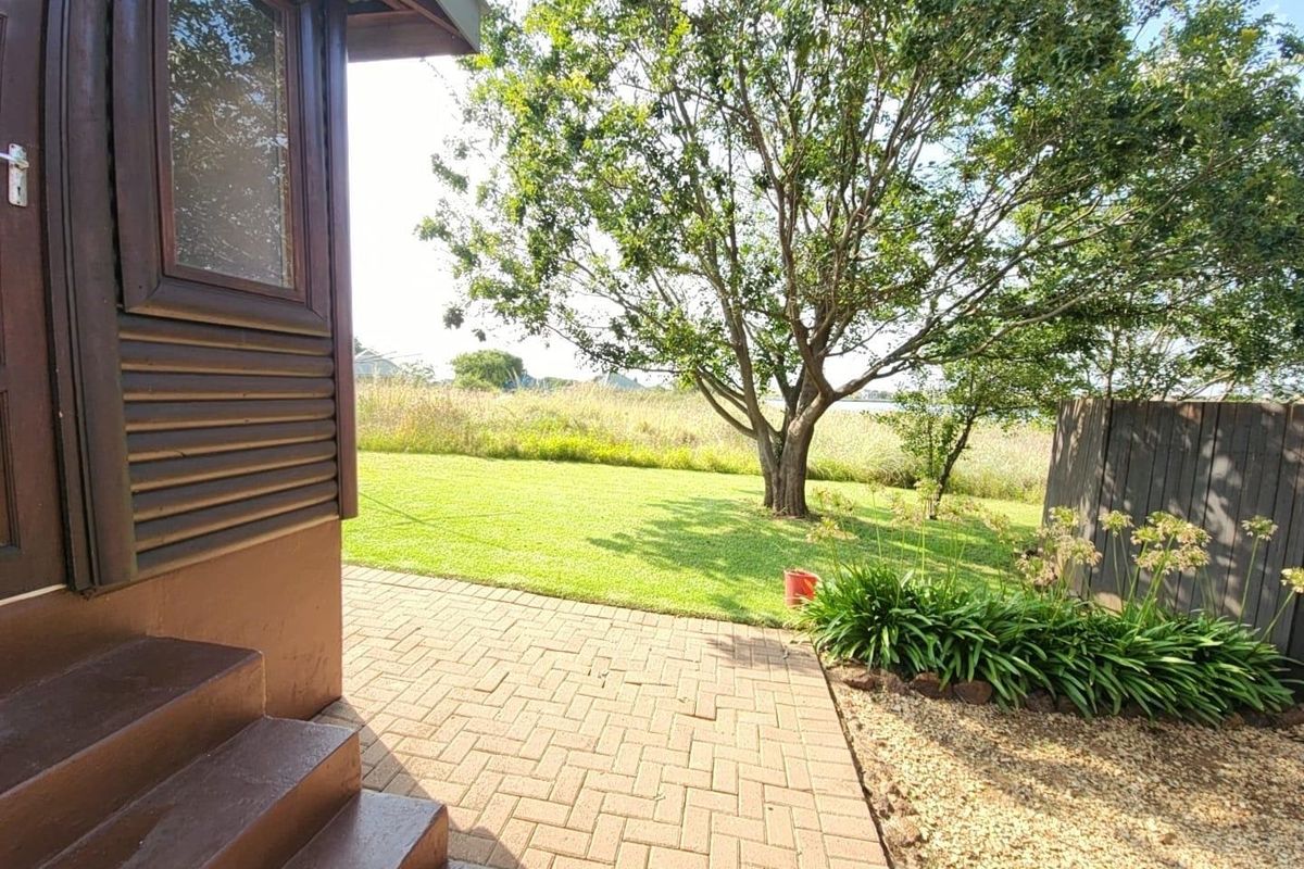 A well-maintained rear garden featuring a paved patio area, timber exterior cladding, and established trees, providing a pleasant outdoor space.