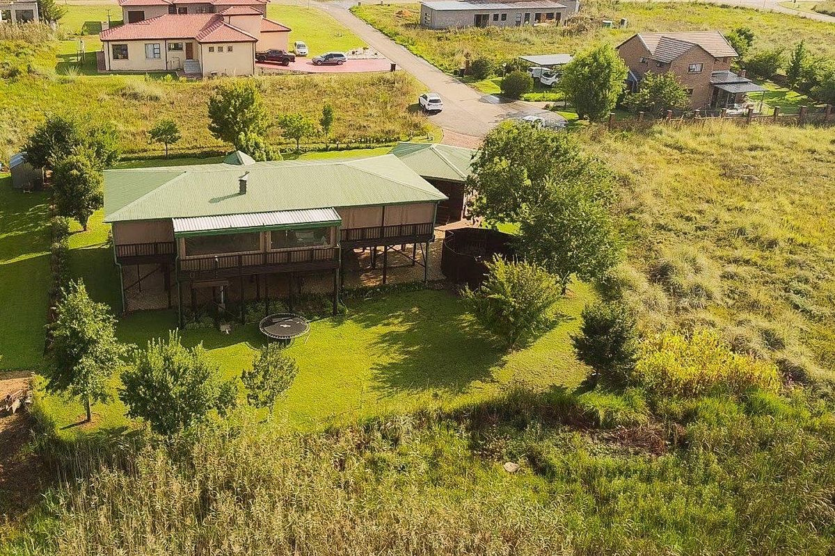 Aerial view of a residential property featuring a raised timber deck, metal roofing, and a spacious surrounding garden area.
