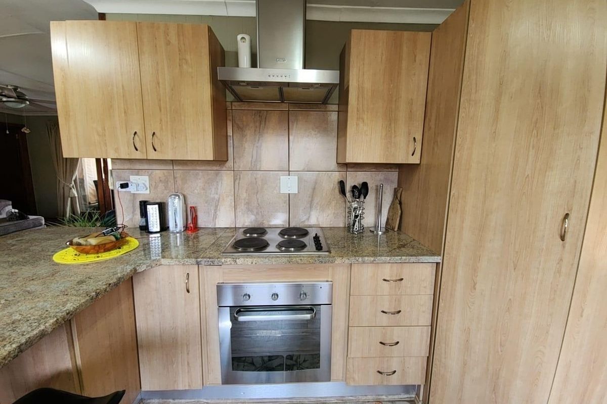 A functional kitchen featuring light wood-look laminate cabinetry, granite countertops, a built-in oven, electric hob, and a stainless steel extractor fan.
