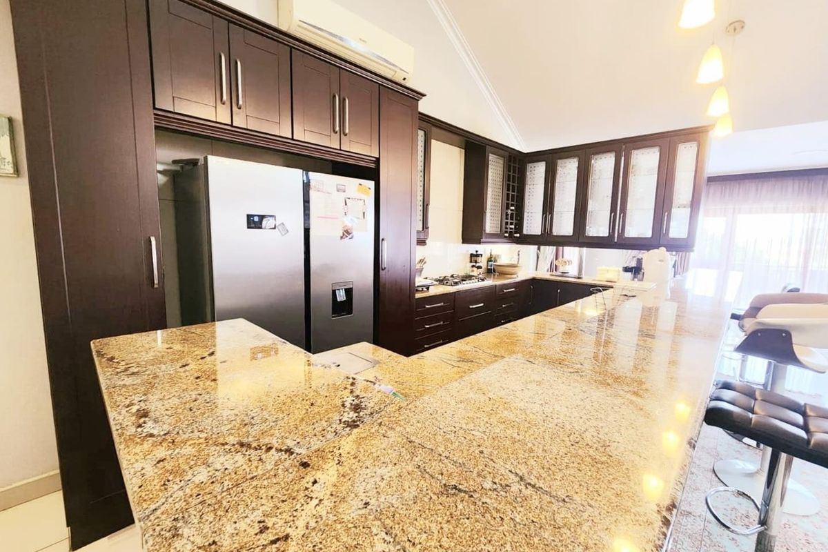 Spacious kitchen featuring dark wood cabinetry, extensive granite countertops, built-in appliances, and a breakfast bar area with pendant lighting.