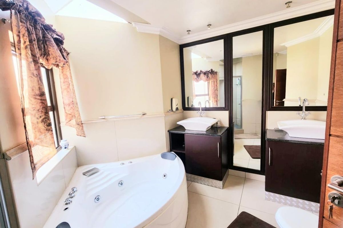 Spacious bathroom featuring a corner spa bath, dual vessel sinks with dark cabinetry, large framed mirrors, and a separate shower enclosure.