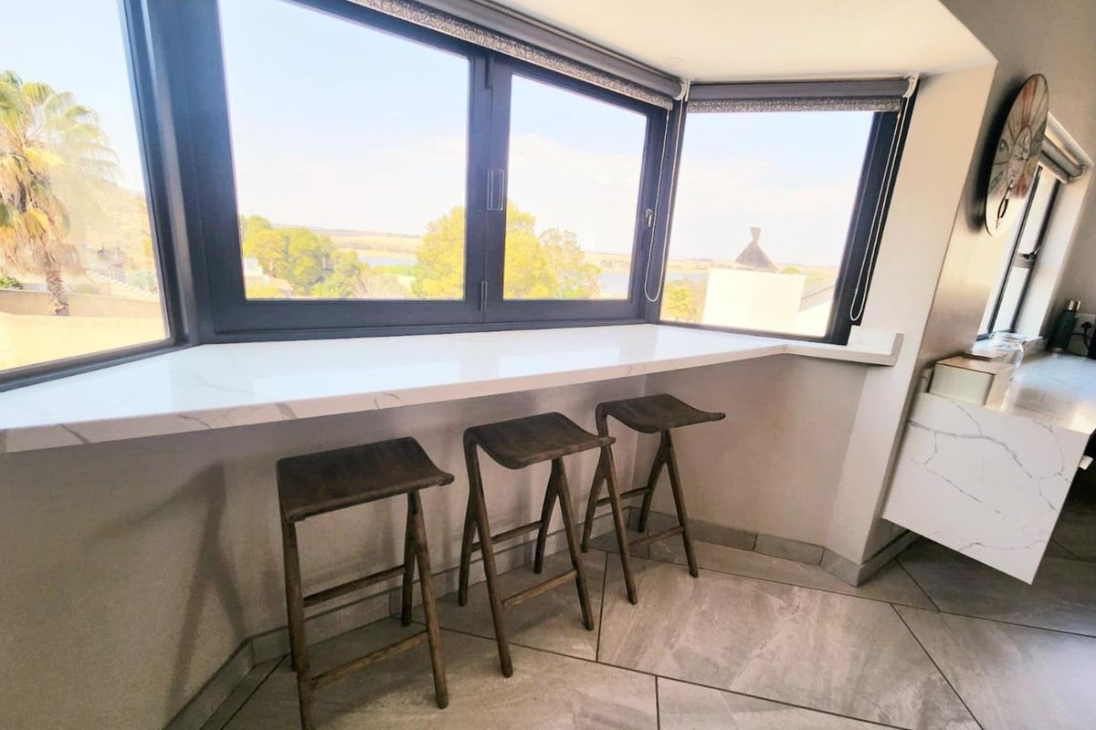 A bright breakfast nook featuring a built-in marble-look countertop, large bay windows with scenic views, and modern tiled flooring.