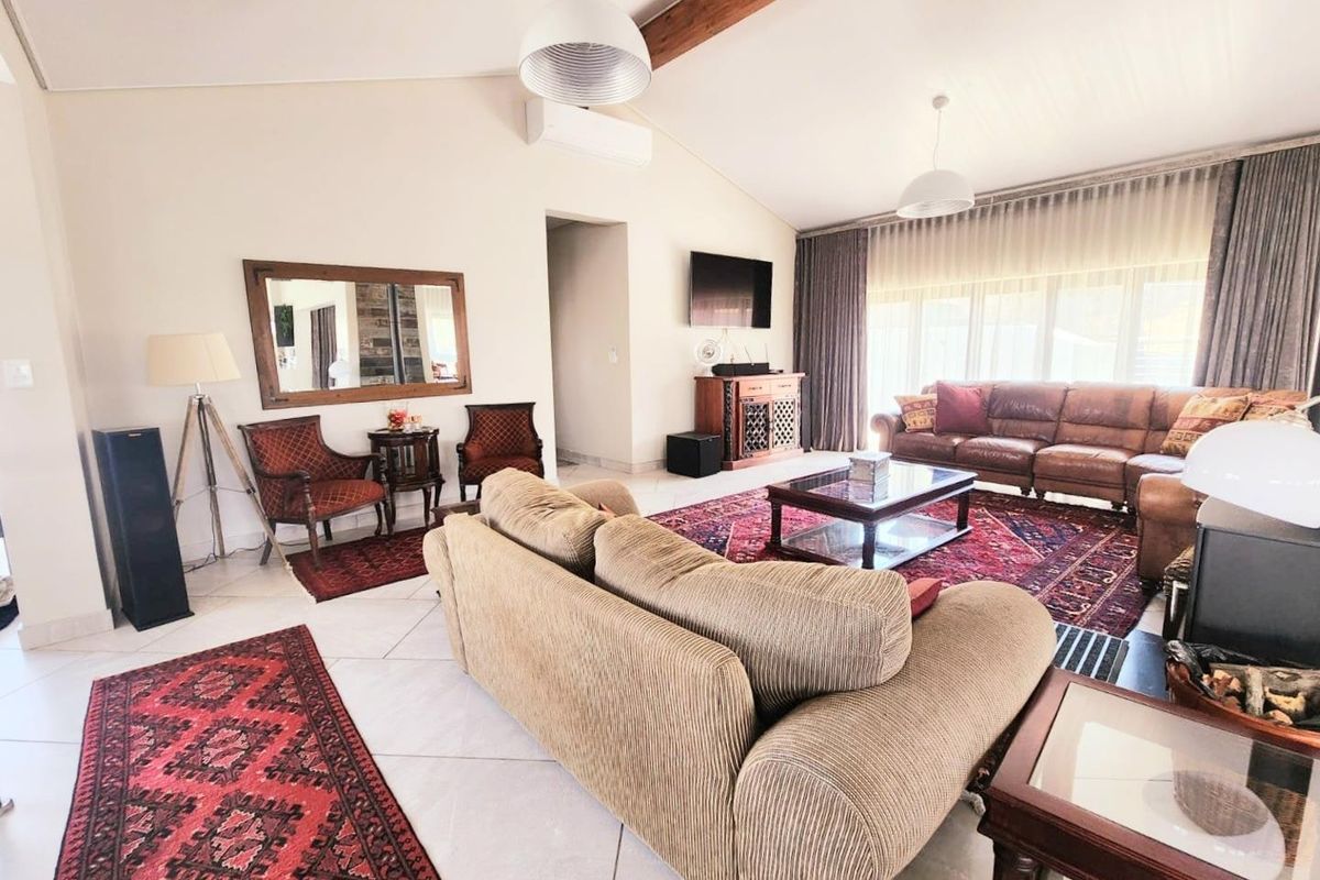 Spacious living room featuring vaulted ceilings with exposed timber beams, large windows with floor-to-ceiling curtains, and neutral tiled flooring.