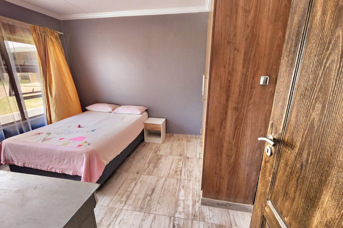 A bedroom featuring tiled flooring, a built-in wooden wardrobe, and coving detail, offering a functional space with natural light.