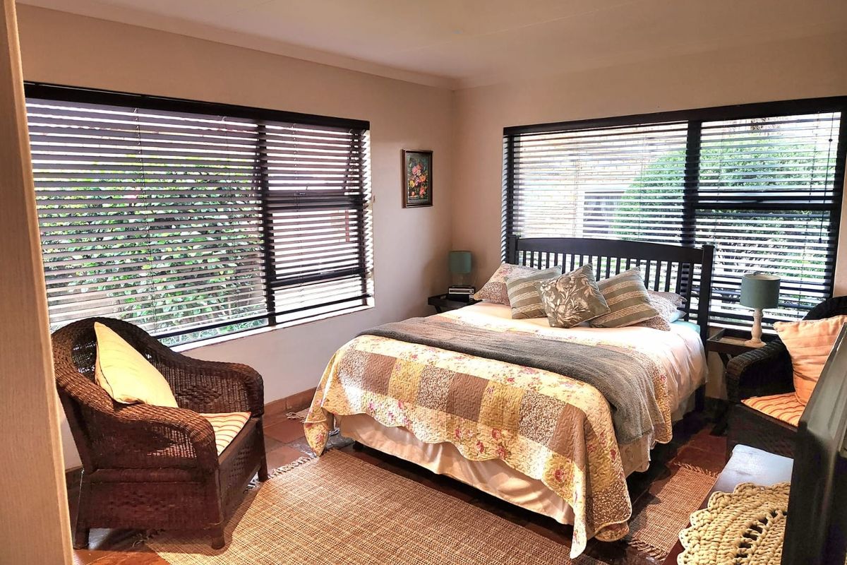 A cozy bedroom featuring dual aspect windows with fitted venetian blinds and terracotta tiled flooring.