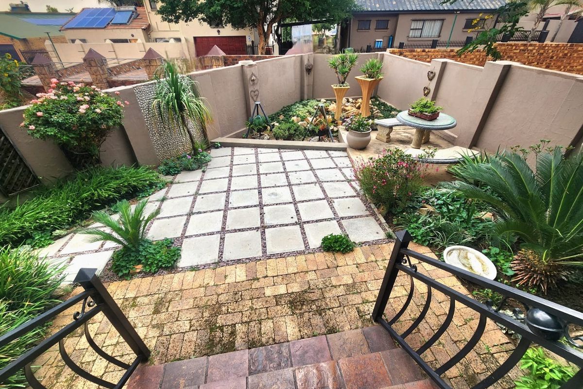 A landscaped rear garden featuring a paved patio area, stone-tiled steps, and enclosed boundary walls, offering a private outdoor space.