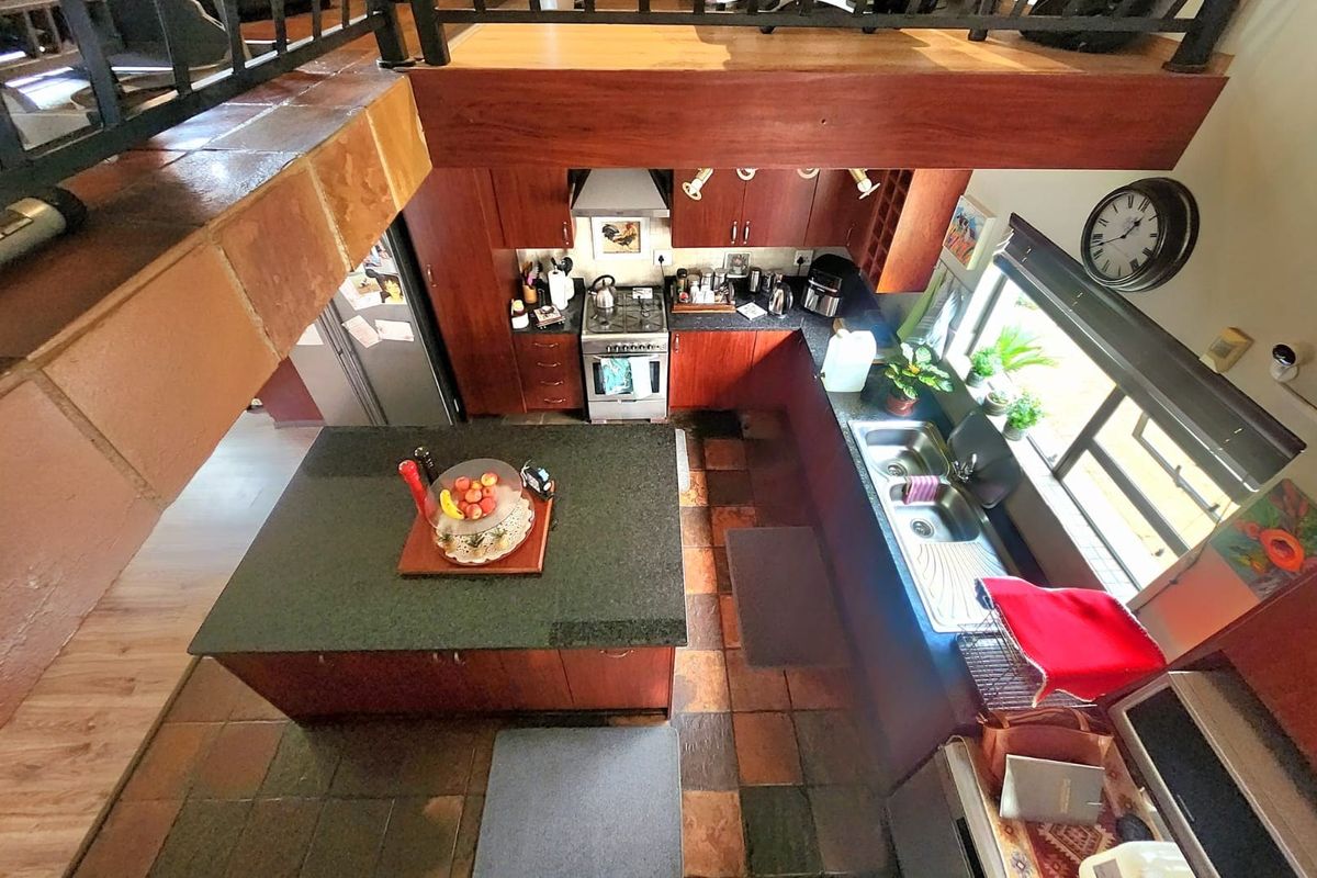 A functional kitchen featuring dark wood cabinetry, a central island with a stone countertop, and a stainless steel gas stove, viewed from an elevated mezzanine.