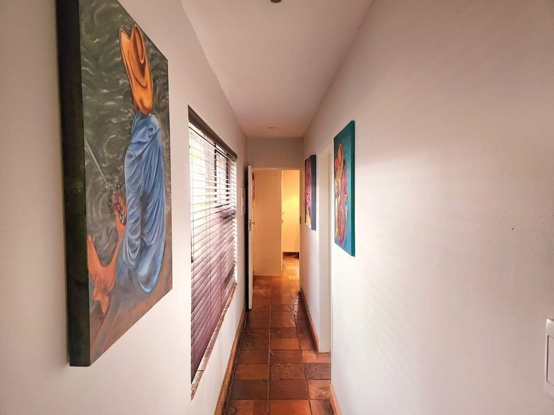 A narrow hallway featuring terracotta-style floor tiles, recessed ceiling lighting, and a window fitted with horizontal blinds.