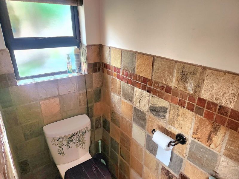 A compact bathroom featuring natural stone wall tiling, a standard toilet, and a frosted window for privacy.