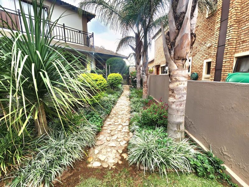 A landscaped side garden path featuring stone paving, mature palm trees, and established garden beds alongside the property boundary wall.