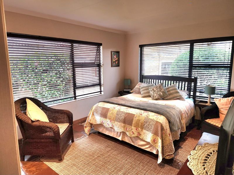 A cozy bedroom featuring dual aspect windows with fitted venetian blinds and terracotta tiled flooring.
