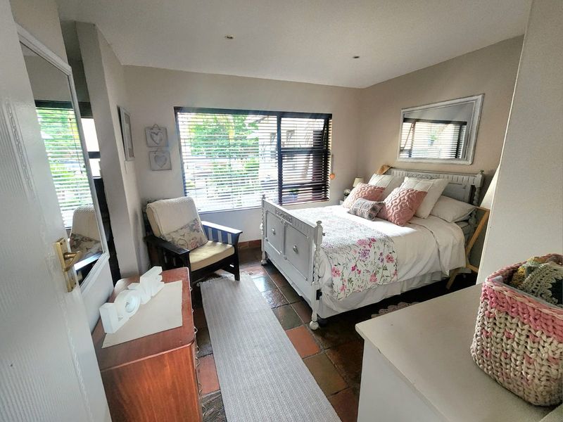A cozy bedroom featuring terracotta floor tiles, recessed ceiling lighting, and a large window with fitted blinds.