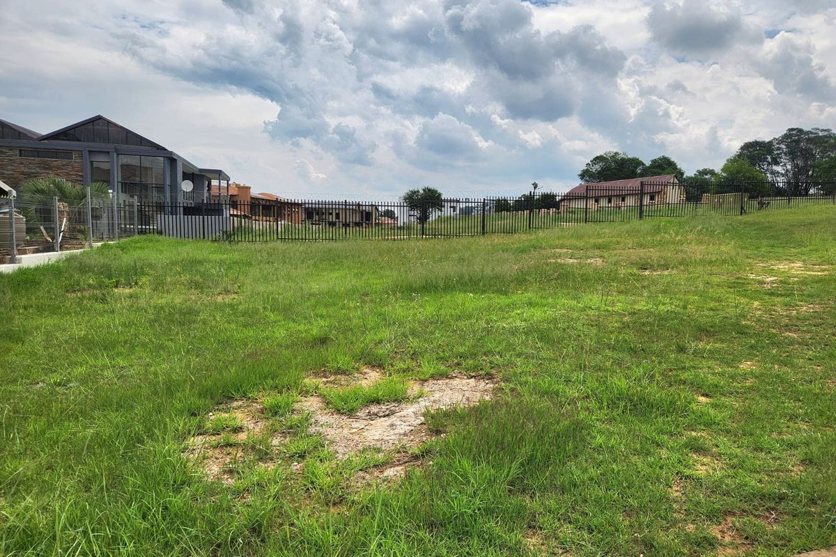 A vacant residential plot featuring established grass cover and secure metal perimeter fencing, situated within a developed residential estate.