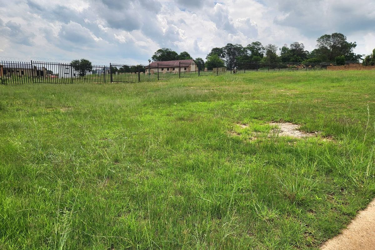 A vacant residential plot featuring open grass land enclosed by perimeter steel fencing with security razor wire.