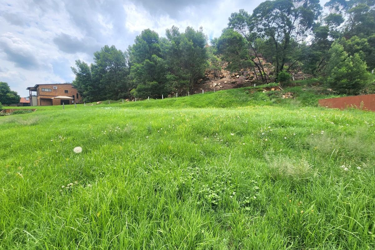 A view of a vacant residential plot featuring sloped grassy terrain, mature trees, and boundary fencing, offering potential for development.