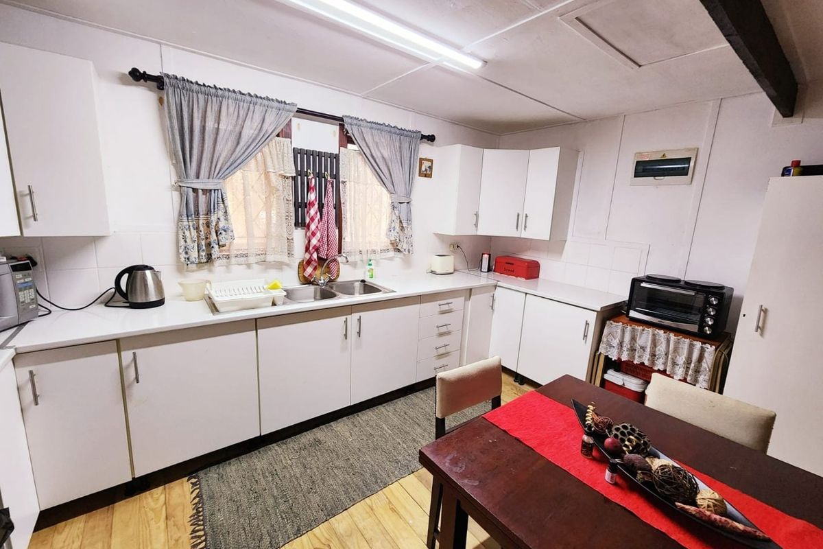 A functional kitchen featuring white laminate cabinetry, double stainless steel sink, tiled splashback, and timber flooring, offering a clean and practical workspace.