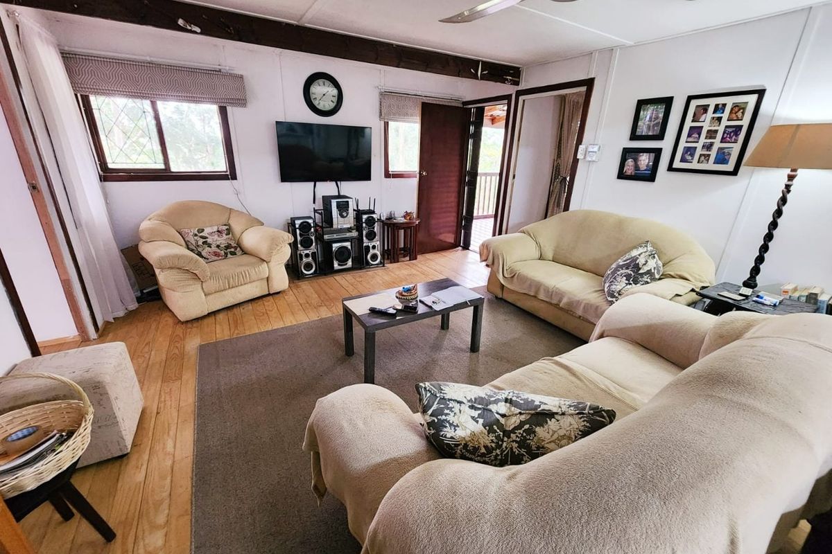 A living room featuring timber flooring, an exposed ceiling beam, and a ceiling fan, offering a functional space with potential for modern updates.