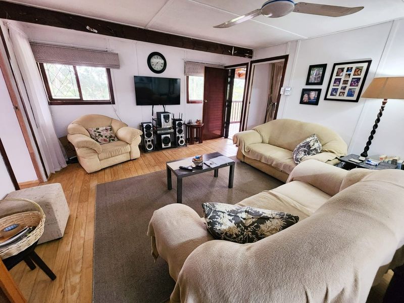 A living room featuring timber flooring, an exposed ceiling beam, and a ceiling fan, offering a functional space with potential for modern updates.