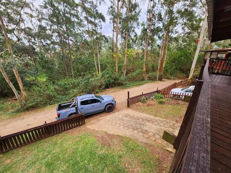 Elevated view of the rear exterior featuring a timber deck, paved driveway area, and surrounding garden with mature trees.
