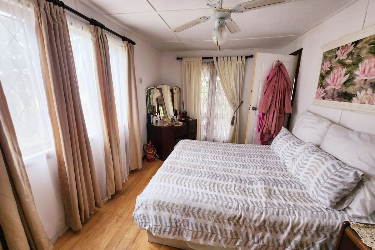 A functional bedroom featuring timber flooring, a ceiling fan, and direct access to an outdoor area through a security gate.