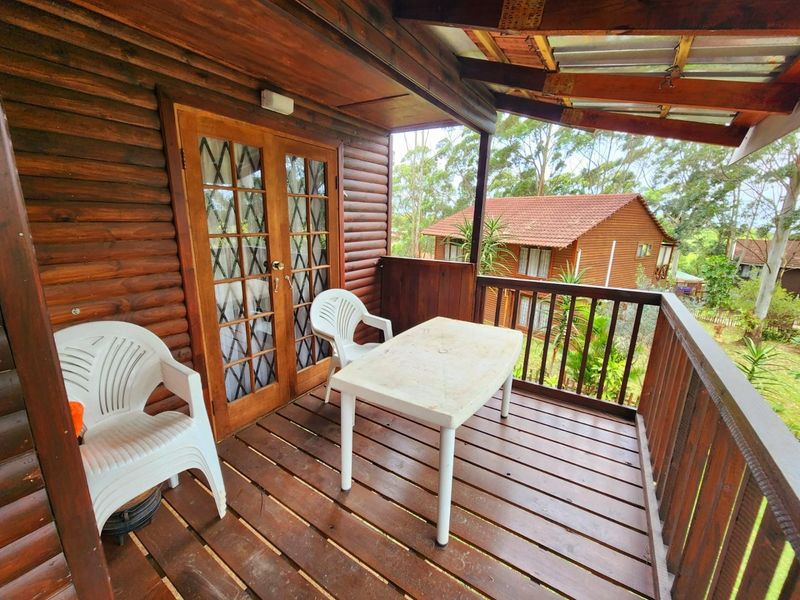 A rustic timber balcony featuring log wall cladding, wooden decking, and a balustrade, offering an outdoor space with a view of the surrounding property.