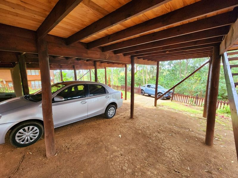 An open-sided carport area featuring exposed timber support beams and posts with an unpaved dirt floor.