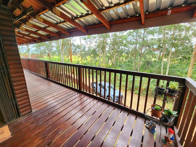 A spacious covered timber balcony featuring exposed rafters and a wooden balustrade, offering elevated views of the surrounding natural landscape.