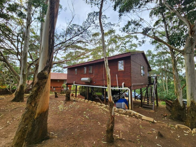 Elevated timber log townhouse featuring an external staircase, under-structure parking, and natural wooded surroundings.