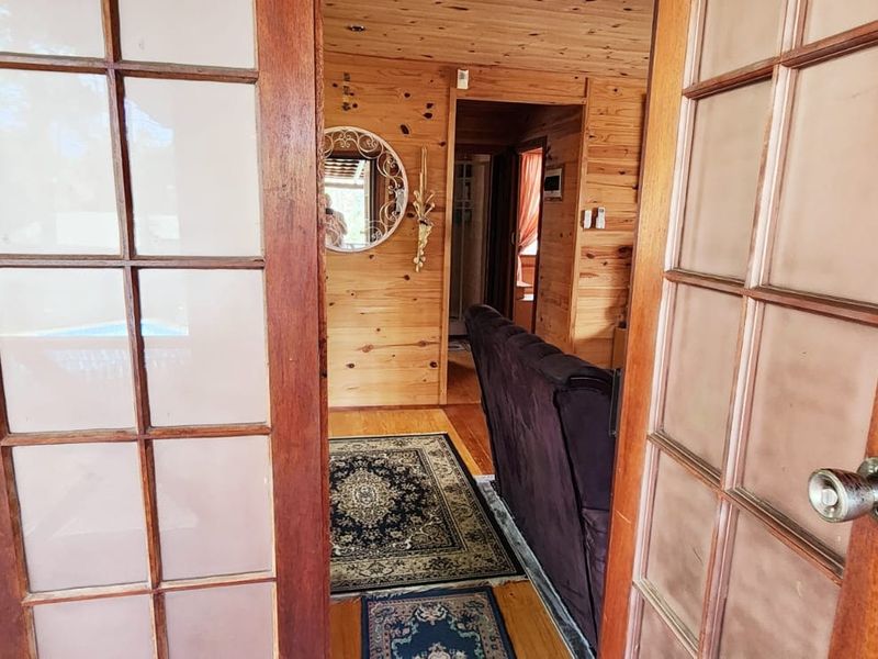 A view through timber-framed french doors into a hallway featuring warm timber wall cladding and flooring, leading towards an adjacent living space.