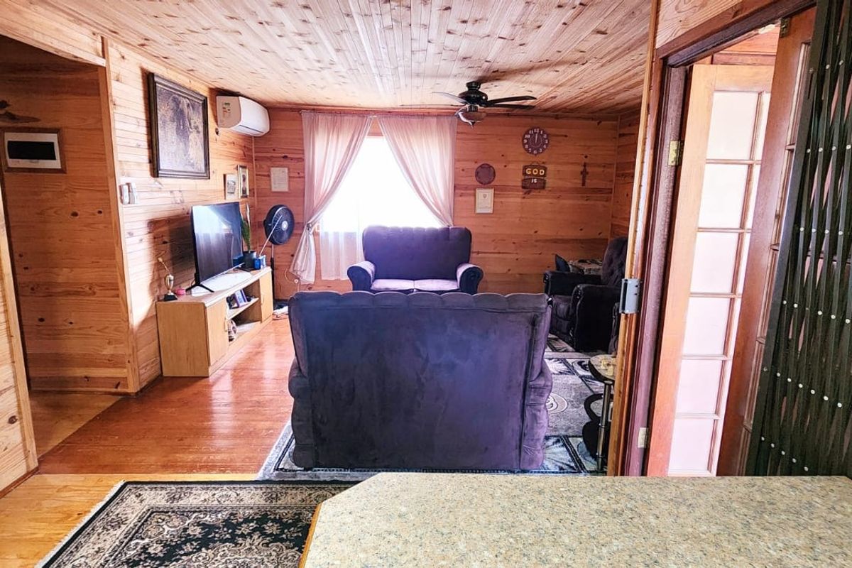 A cozy living room featuring extensive timber wall and ceiling cladding, timber flooring, a ceiling fan, and a wall-mounted air conditioning unit.