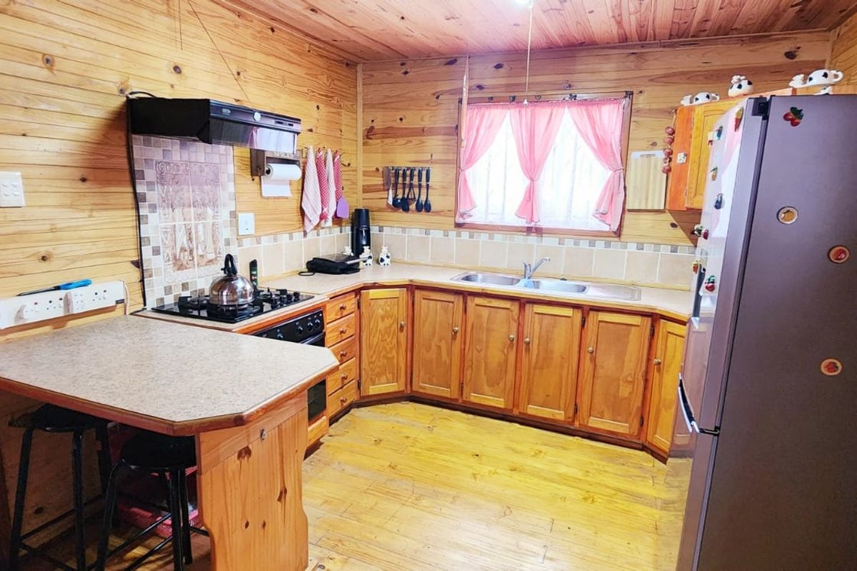 A rustic kitchen featuring timber wall and ceiling cladding, wooden cabinetry, laminate countertops, and a gas hob with an extractor fan.