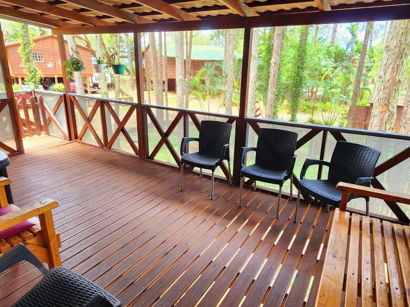 A covered timber deck patio featuring wooden balustrades and screened walls, offering an elevated view of the surrounding wooded garden area.