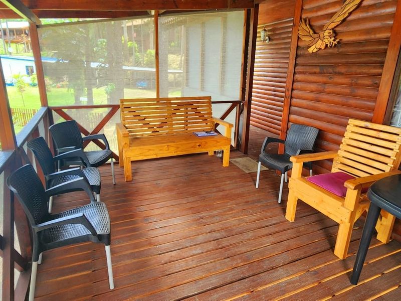 A covered timber patio featuring wooden wall cladding and a screened enclosure, overlooking the garden and pool area.