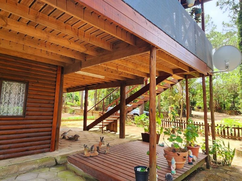 A covered outdoor patio area featuring timber decking, exposed wooden beams, and an external staircase leading to the upper level of the log-style townhouse.