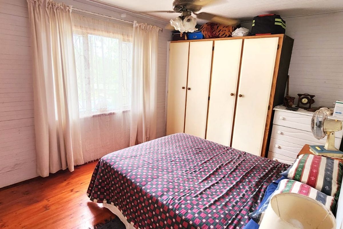 A bedroom featuring timber flooring, a built-in wardrobe, and a ceiling fan, offering a functional space with classic finishes.