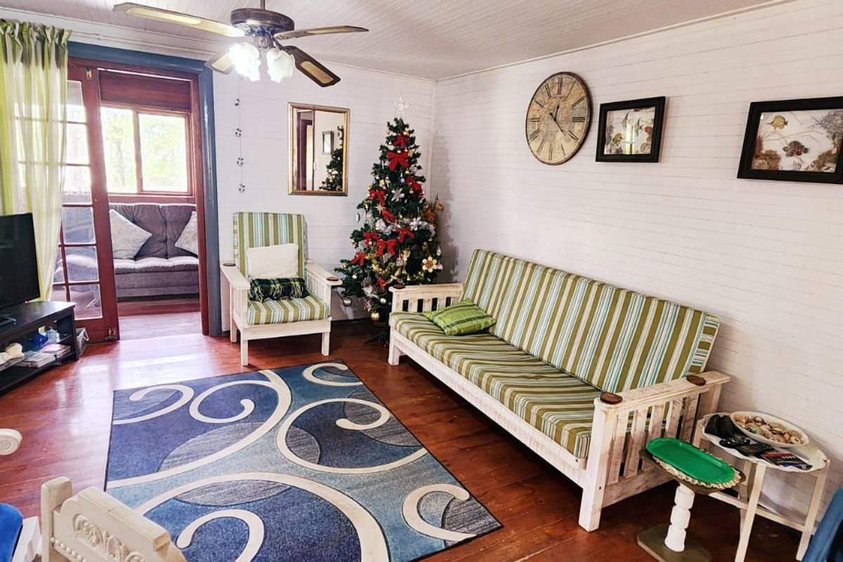 A cozy living room featuring timber wall panelling, polished timber flooring, and a ceiling fan, with direct access to an adjoining patio area.