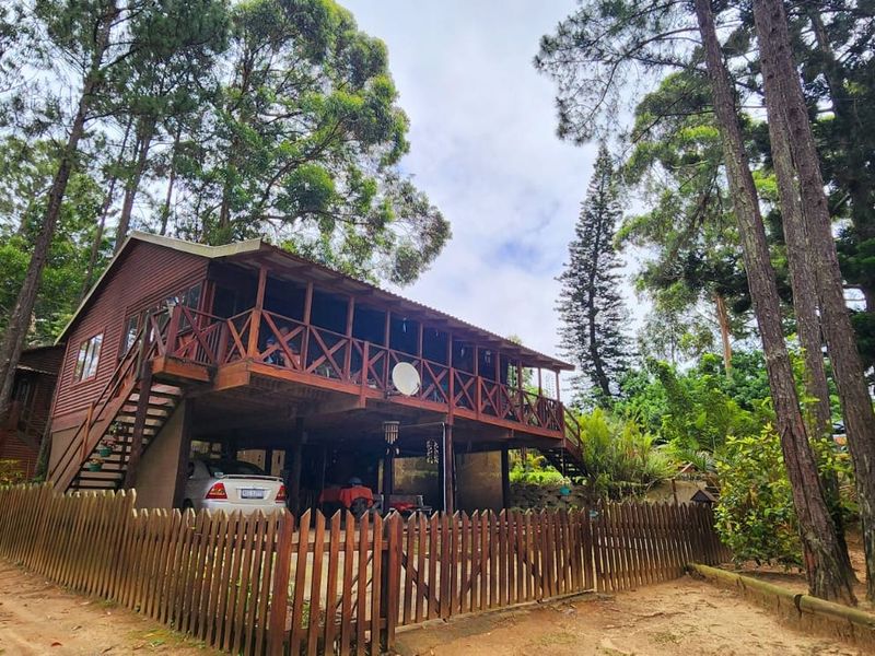 A rustic timber townhouse featuring a raised deck, external staircase, and a wooden picket fence, set within a wooded environment.