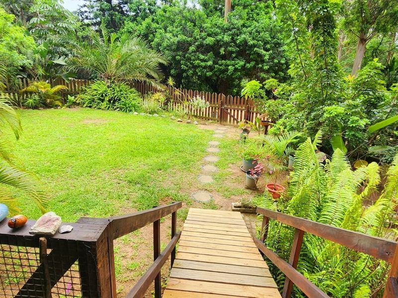 A lush, private garden featuring a wooden staircase leading down to a well-maintained lawn, surrounded by mature trees and foliage.