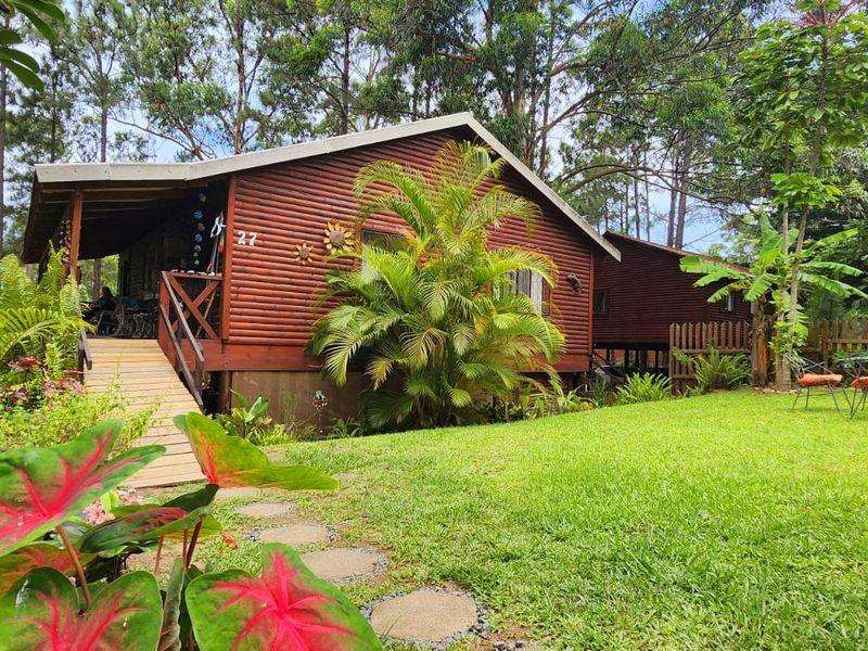 A charming timber log townhouse featuring a covered deck, wooden staircase, and a lush, well-maintained garden setting.