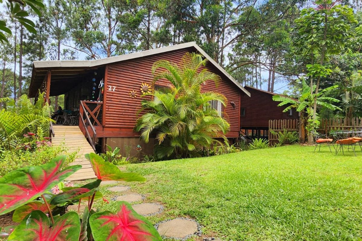 A charming timber log townhouse featuring a covered deck, wooden staircase, and a lush, well-maintained garden setting.