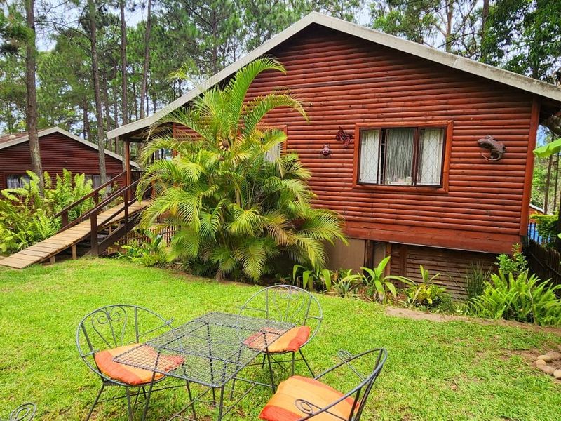 A view of the rear exterior of a log cabin style townhouse featuring a raised timber staircase and a lush, landscaped garden setting.
